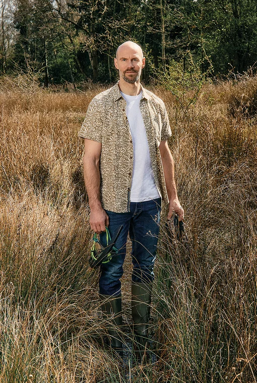 Mann steht mit Hemd und Jeans im Moorwasser