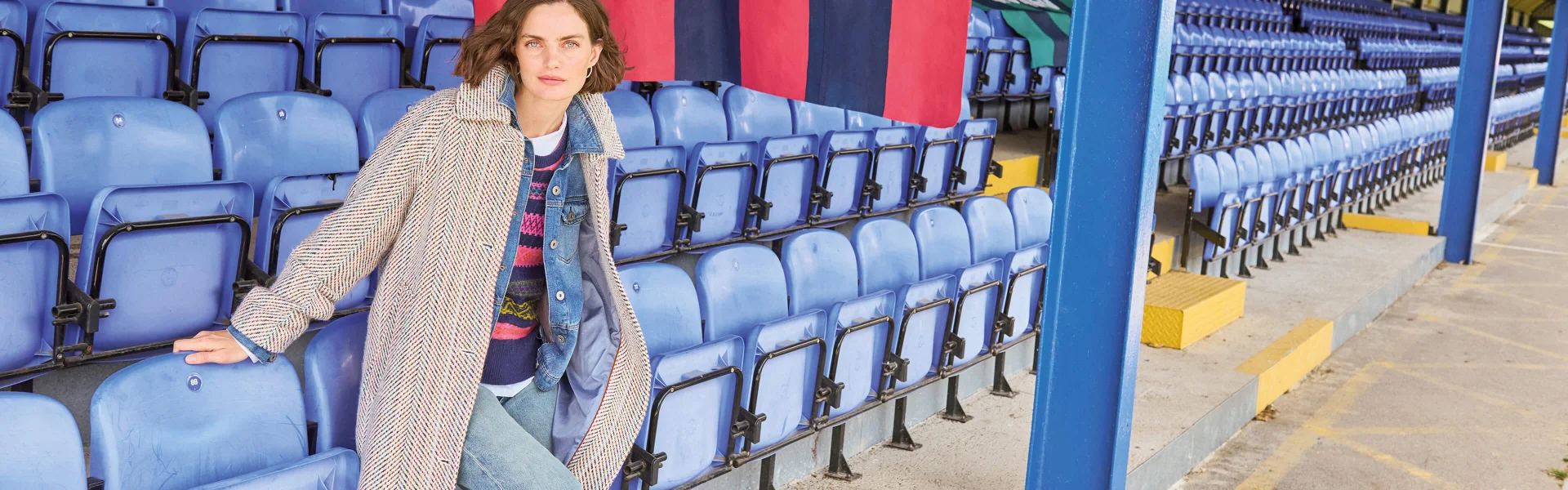 Frau, die sich auf blaue Sitze lehnt und einen langen beigefarbenen Mantel trägt